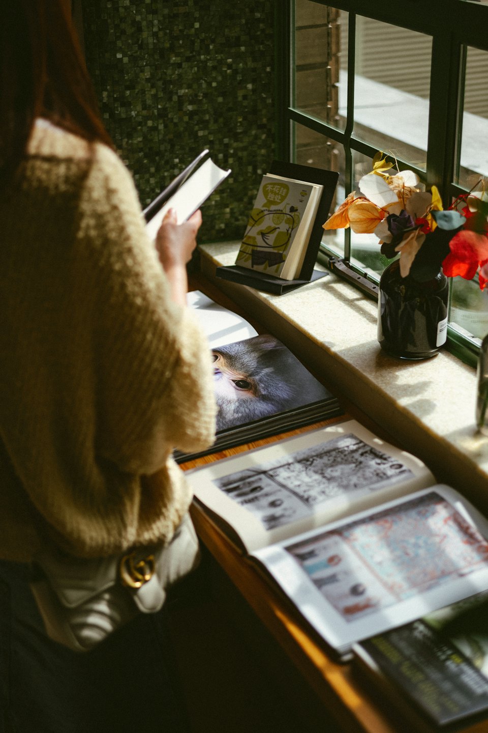 Eine Person liest ein Buch am Fenster mit Blumen.